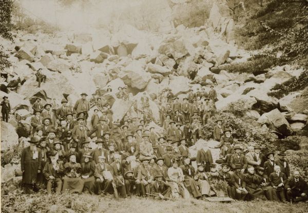 Outdoor group portrait of a reunion of the Iron Brigade, veterans of the Civil War, and their families at Devil's Lake, Wisconsin. 

The couple seated in the first row, second and third from the right, are Colonel and Mrs. Cornelius Wheeler of Portage, Wisconsin. Colonel Wheeler (1840-1915) served in Company I of the 2nd Wisconsin Volunteer Infantry from 1861-1864, and was later Governor of the Northwest Branch of the National Soldiers' Home in Milwaukee from 1892 to 1915.