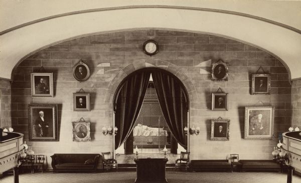 Interior view of Washington and Lee University chapel showing tomb of Robert E. Lee. Portraits hang on the wall around an arch leading to the tomb.