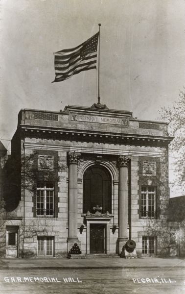 Exterior of the Grand Army of the Republic Memorial Hall. There are a mortar and cannon balls near the front columns flanking the entrance, and a large American flag flying from the roof.
