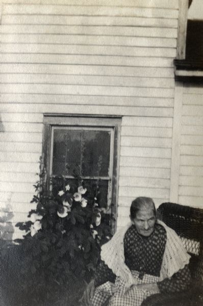 Brigit O'Keefe Quinney, Richard Quinney's great grandmother, sitting next to the family's farmhouse and flowering hollyhocks.