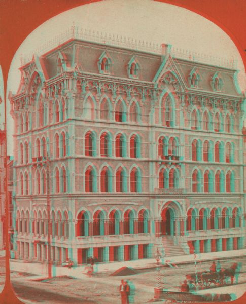 Stereograph; corner of Broad and Wisconsin Avenues. Built in 1870.  E.T. Mix, architect. Victorian details decorate the six story building. A small pile of dirt is in the road. Pedestrians are on the sidewalks, and two horse-drawn carts, one reading "Piano Mover," are in the lower right.