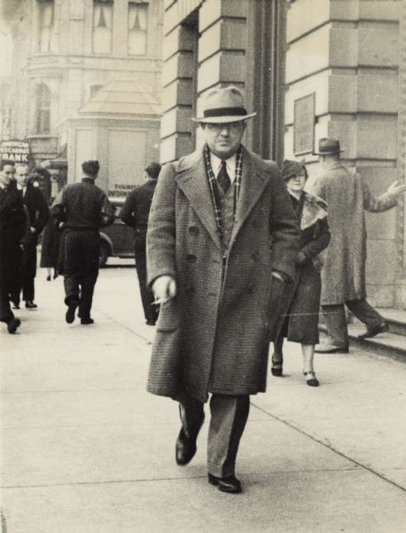 Leon Lamoreux walking down the sidewalk on South Pinckney Street, Capitol Square. The building on the right is the First National Bank (now the "glass" bank). There is an information booth and American Exchange Bank in the background. Leon, and his wife Beatrice, later taught typing and telegraphy to Naval students at the U.S. Naval Training School (Radio) in Madison.