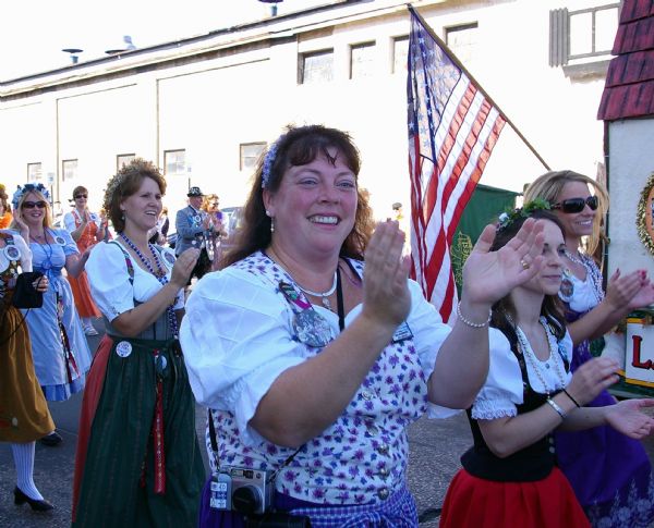 Women in costume smiling and clapping in Oktoberfest parade.
