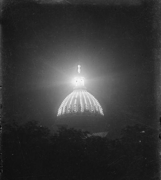A night view of the dome and lantern of the third Wisconsin State Capitol, lighted with electric lights.