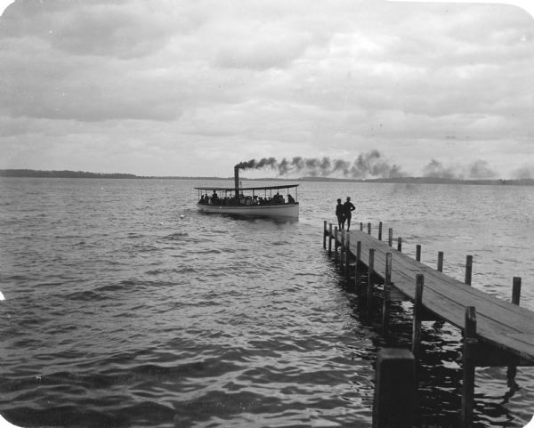 The lake steamer "Alice" approaches the Madison dock on Lake Monona.  Two boys wearing caps stand at the end of the pier. At the time of this photograph, the Askew Brothers operated the "Alice" and three additional steamers: "Tonyawatha," "Winnequah," and "Monona A."