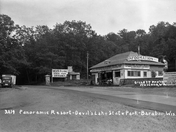 View of the entrance to Devil's Lake State Park. There is an information center offering gas, food, and Blatz beer. Two storekeepers and a boy sit on the porch. Over the entrance to the information center is a sign that says: Panoramic Resort Hotel and Cottages with Bath, Gas, Hot and Cold Water. Rates $1.00 and Up."
