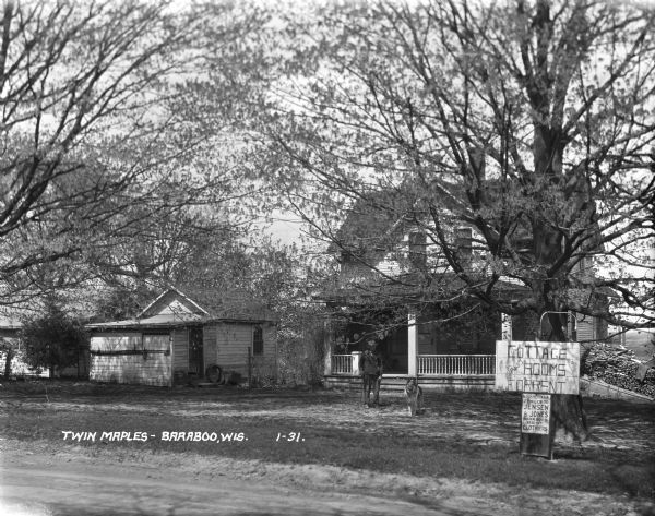 A man and his dog are on the lawn in front of a house. A wooden sign reads, "Cottage and Rooms for Rent." Another sign below advertises for "N.F. Sherman 2 [?]/10 miles to Jensen & Jones Baraboo's Best Clothiers".
