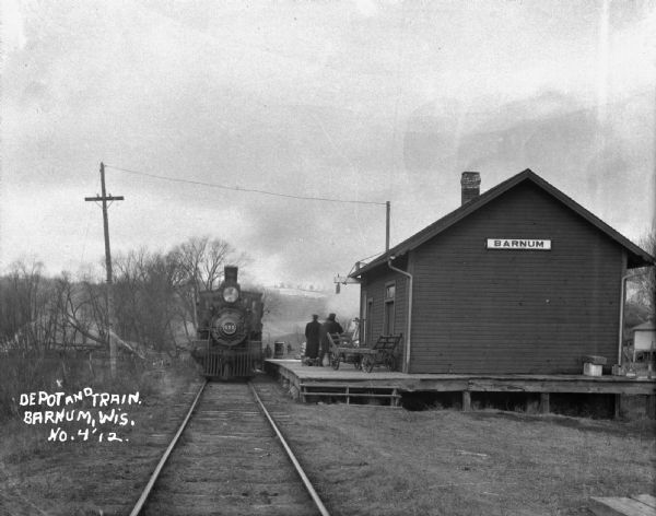 View down railroad tracks of a locomotive arriving at the Barnum Depot.
