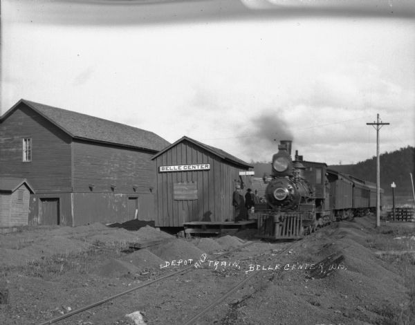 Exterior view of a locomotive at the Bell Center depot. Men stand on the platform.