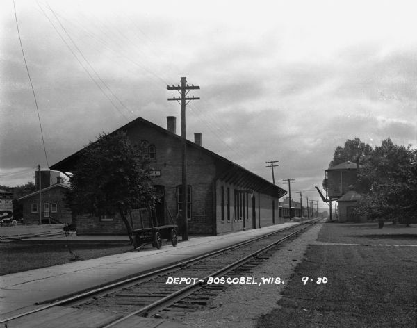 Boscobel Depot View across railroad tracks of the Boscobel train depot. A wagon is parked on the platform. There is an advertisement for the circus painted on a wall at the far left.