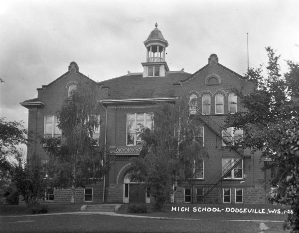 Facade of the three-story high school. There is an open cupola on the roof.