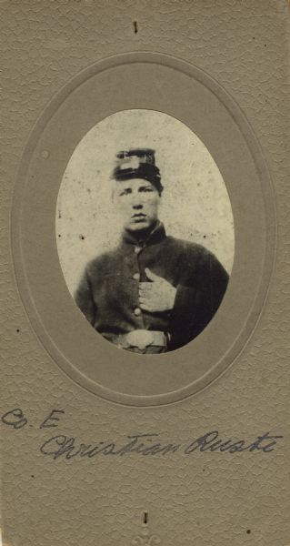 Waist-up oval studio portrait of Christian Ruste, a private in Company E, 15th Wisconsin Infantry in uniform. The following information was obtained from the Regimental and Descriptive Rolls, Volume 20: He resided in Blue Mounds, Wisconsin. On January 8, 1862, he enlisted at Camp Randall in Madison, Wisconsin and was mustered into service in Madison, Wisconsin on January 11, 1862, at the age of 17. He died on May 2, 1862, at Island No. 10 (Tennessee) of Typhoid fever.