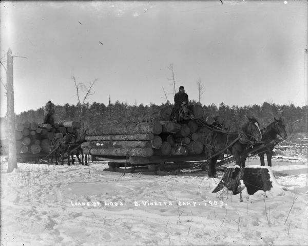 Two sled loads of logs each drawn by teams of two horses at Bruno Vinett's logging camp. Drivers sit atop the loads. The ground is covered with snow.