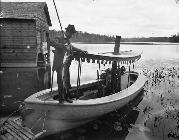 Steamboat on Long Lake owned by Lorenzo Newman of Chippewa Falls. It is anchored at Newman Peninsula on Long Lake near a wet boathouse. The boat was operated by steam and used as an excursion boat. It had cushioned seats, electric lights and a canvas canopy. In the background is the far shoreline of the lake.