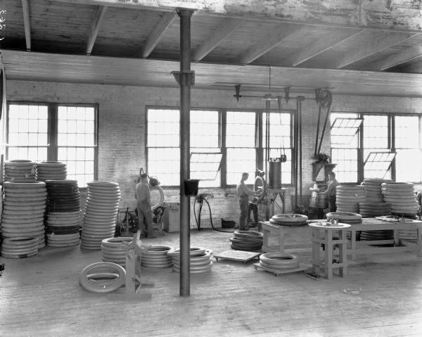 Three men use three different pieces of machinery in various stages of the tire-making process at the Boone Tire Factory. Stacks of tires are piled around the room.