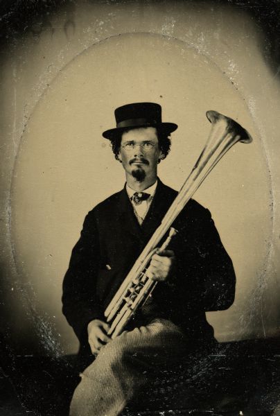 Tintype portrait of Joseph Smith of Evansville, Wisconsin, member of the 3rd Wisconsin Infantry band. He is seated wearing a suit and holds a tenor horn.