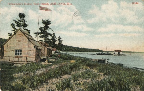 View of several fisherman's homes on Bear Island, one of the islands that make up the Apostle Islands. An American flag is flying between buildings and a dock, boat, and boathouse are in the distance.