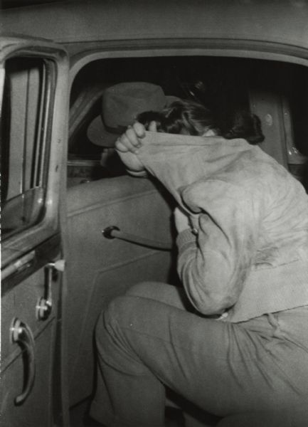 View of a woman as she was loaded into the agent's car after a raid at Rae's Blackhawk Bar. She is hiding her face in her coat.