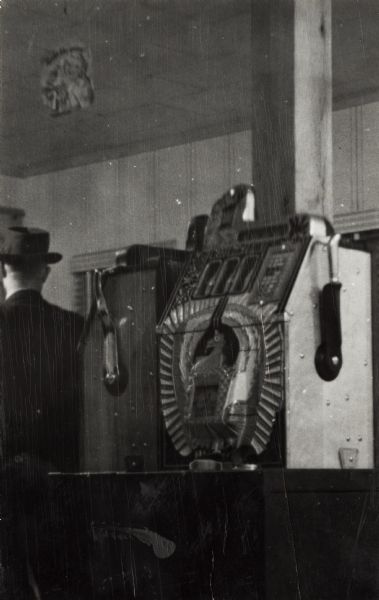 Two illegal gambling machines in a tavern on Highway 41, about one mile south of the Racine County Line. A man in a hat stands on the left, facing away.