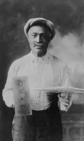 Portrait of Henry Mathews, 1866-1941, an early African American resident, holding the tools of his trade in front of a painted backdrop. He was a stone mason for many years.