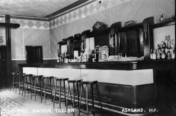 Interior view of the bar, with eight bar stools. Signs behind the bar include "Coca-Cola," "Grain Belt Beer," "Goebel," and "Pabst Blue Ribbon Beer."