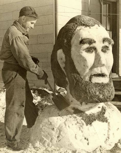 A man uses a shovel to carve out a large bust of Abe Lincoln out of snow.