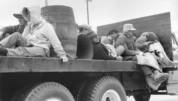 Transporting Migrant Workers Chicano migrant farm workers being transported to a field on a cold Texas winter morning on the back of a truck. This photograph is a part of Wisconsin-native David Giffey's series "Struggle for Justice," images from the migrant farm worker struggle including an independent organizing effort in Wisconsin and the nationwide grape boycott movement started by Cesar Chavez of United Farm Workers during the 1960s and 1970s. Many migrant farm laborers traveled from Texas to Wisconsin in search of seasonal field work. <p></p>Transporte para trabajadores emigrantes <p></p>Transporte para trabajadores agrícolas emigrantes de origen chicano detrás de un camión yendo hacia un campo durante una mañana fría de invierno en Texas. Esta fotografía es parte de la serie "Lucha por la Justicia" tomada por David Giffey, originario de Wisconsin, las imágenes muestran la lucha de los trabajadores agrícolas emigrantes incluyendo un esfuerzo independiente organizado en Wisconsin y el movimiento nacional del boicot de uvas empezado por Cesar Chávez de la unión de campesinos o United Farm Workers durante los años 1960 y 1970. Muchos obreros agrícolas emigrantes viajaban desde Texas hacia Wisconsin en busca de trabajo temporal en los campos.