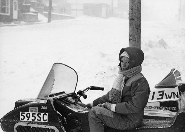 Winter scene with young woman on a snowmobile in downtown Theresa, Wisconsin.
"Kathy Thompson, daughter of Arty Thompson, rides a snowmobile during the height of the storm."