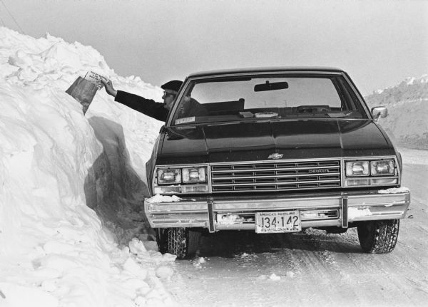 Winter scene with mail carrier in car putting mail in a mailbox.  "Ralph Koll, Rural Mail Carrier. Somewhere in this monstrous snow drift is Helen Moldenhauer's mail box. Ralph Delivers to 264 boxes on his 63.6 mile route. In eighteen winters of mail delivery, Ralph reports that this winter was the most severe."