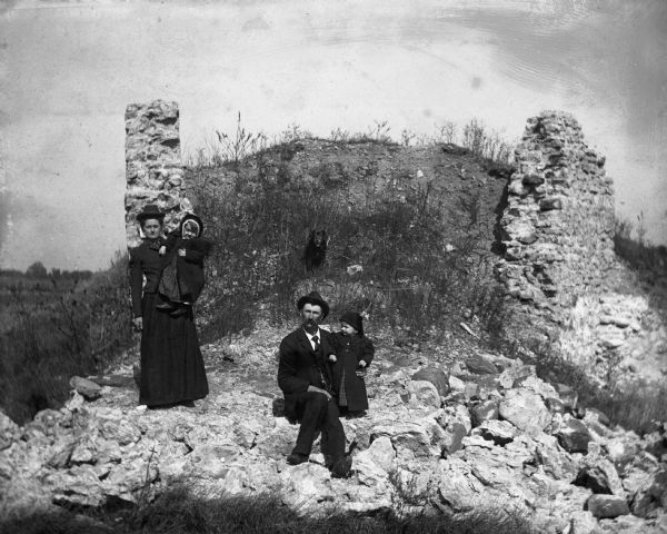 Portrait of the Alex Krueger family by lime kiln ruins. Florentina is standing holding and Jennie, Alexander is sitting with Edgar, and Rover, the family dog, is sitting behind them.