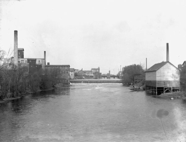 View of the Globe Milling Company, built in 1848, and the Lewis Factory on the Rock River. In the distance is a dam, bridge, and barbershop.