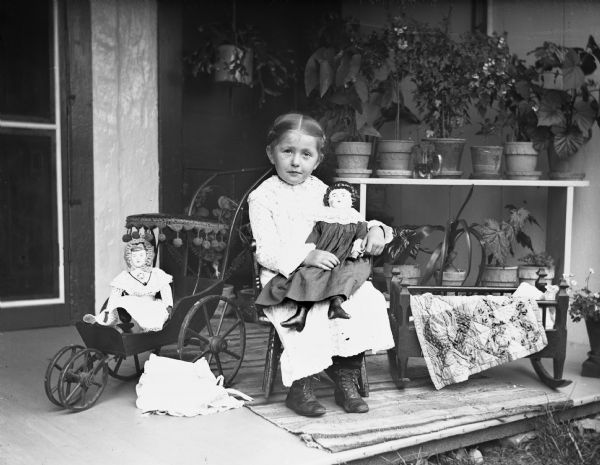 Young Jennie Krueger, the photographer's daughter, sitting with her dolls on the porch.