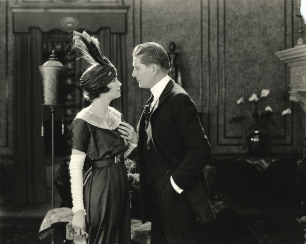 Justine Spotiswood (played by Irene Castle wearing a turban with feathers) and Cosmo Spotiswood (William P. Carleton) gaze into each others eyes in a scene still from the silent film "The Amateur Wife" (Lasky 1920).