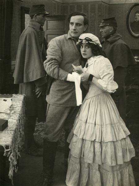 William Clifford and Ethel Grandin in 1860s or 1870s period costume. They are apparently being guarded by two U.S. Army soldiers in this scene still for "Across the Plains" (Bison 1912).