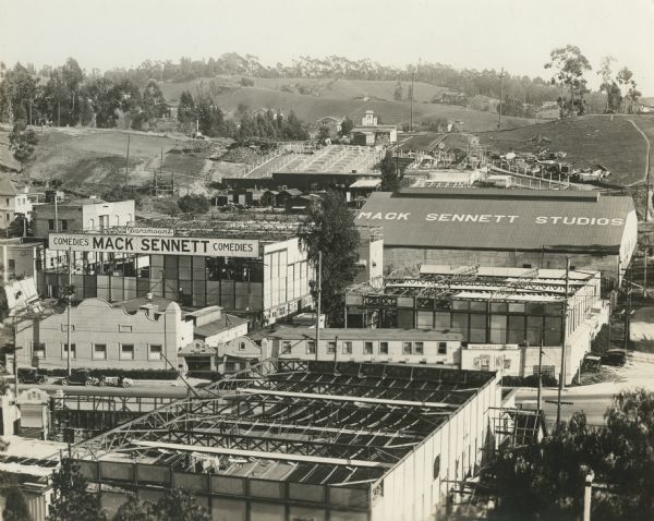 Elevated view of the Max Sennett Studios. There are many open-roofed studios with cloth diffusers. A huge sign reads: "Paramount-Comedies-Mack Sennett-Comedies." Paramount Pictures distributed Sennett's silent films from 1917 to 1921. The present address of the site is 1712 Glendale Boulevard, Echo Park, California.