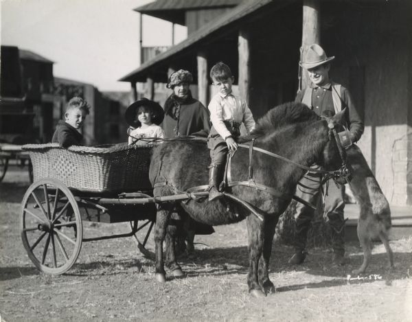 Original caption: "Mr. and Mrs. Will Rogers, their three children and the pony and cart which was recently purchased for their enjoyment. Jimmy, who supported his dad in several pictures is seen astraddle the pony."