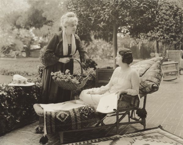 Clara Kimball Young and Pauline Maddern Kimball Pauline Maddern Kimball, holding a basket of flowers, shows a bouquet to her daughter, the silent film star Clara Kimball Young who is on a chaise lounge with what appears to be a copy of "Vanity Fair" magazine in her hand.