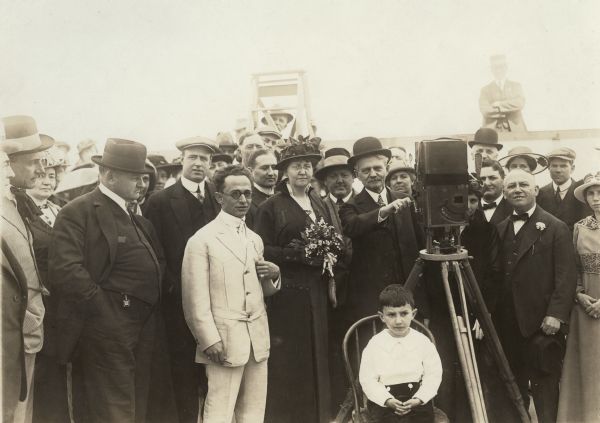Gathered for the grand opening of Universal City are the general manager of the Universal Film Manufacturing Company, Isadore Bernstein (in a white belted Norfolk suit and round sunglasses); the company's president, Carl Laemmle (to the right of the camera in dark suit with carnation boutonniere); and very probably the seven-year-old Carl Laemmle, Jr., seated in front wearing a white shirt. An unidentified man has his hand on the crank of a Prevost motion picture camera.