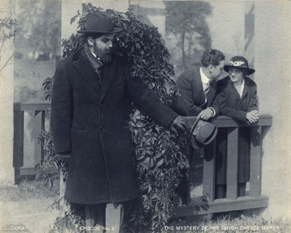 Hassam Ali (played by James Cruze) is evesdropping from behind a bush on his neice Zudora (Marguerite Snow) and John Storm (Harry Benham) in a scene still from the Thanhouser serial "Zudora." The print is captioned "Episode No. 3" and "The Mystery of the Dutch Cheese Maker."
