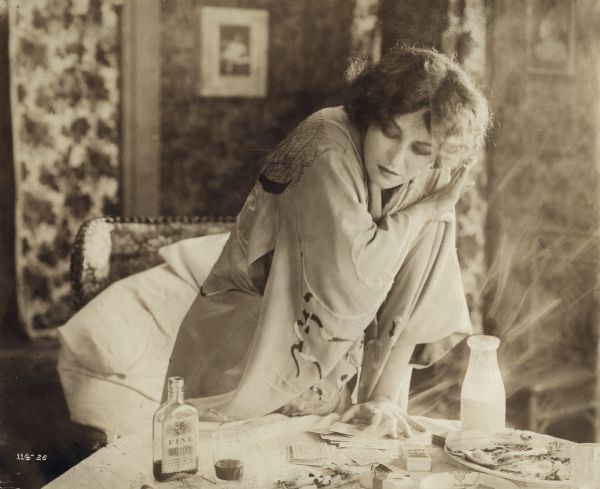 Pauline Frederick as Myra, wearing a kimono, reacts to the signs of her dissipation scattered on a table: playing cards, cigarettes, whiskey, the remains of a meal.
