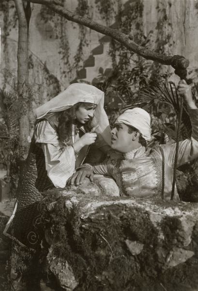 Faimeh Fitzgerald (played by Edith Storey) cautions Jack Stanton (Antonio Moreno) as he hangs on the rope of a well in a publicity still for "Aladdin from Broadway." They are in Turkish costumes with Moreno wearing a turban and Storey a headscarf.