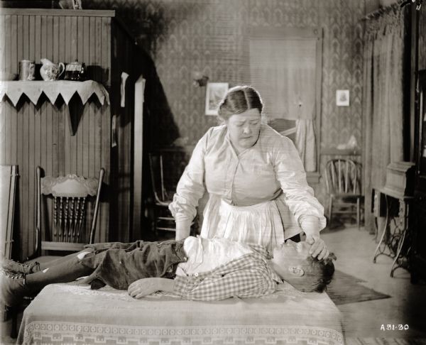 Mrs. Americus Jenkins (played by Kate Price) nurses her sick son (Wesley Barry) in a tenement set for the silent film "Amarilly of Clothes-Line Alley."