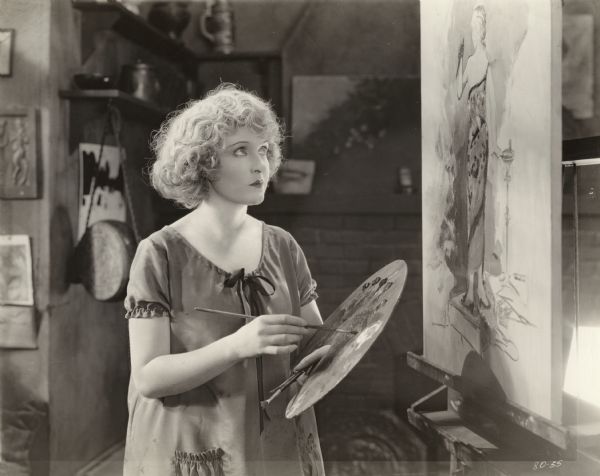Theodora "Teddy" Hayden (played by May Allison) works on an oil painting with palette in hand in a scene still for the 1920 Metro silent film "Are All Men Alike?"