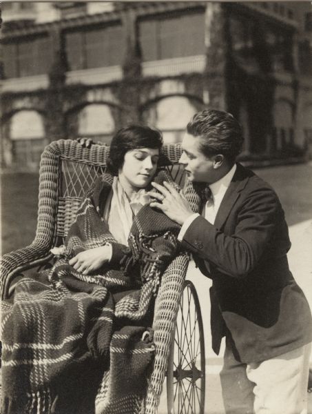 In this scene still for "The Artist's Wife," the young artist Adair (played by Elmer Clifton) kneels beside the wicker wheelchair of his model Jean (Miriam Cooper).