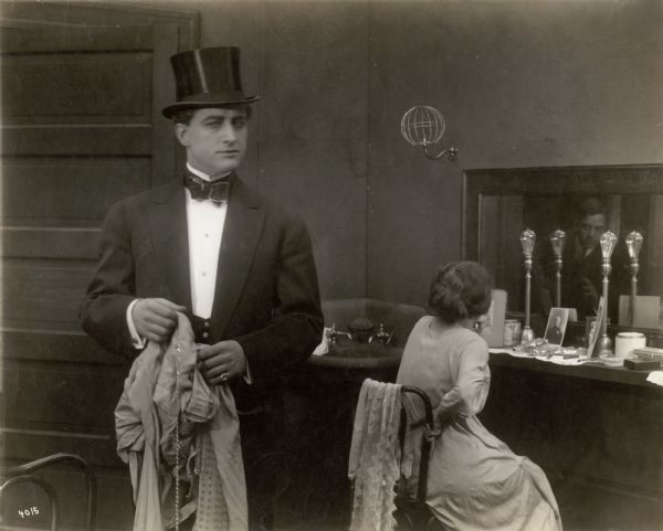 Fred Willard, a theatrical manager played by Francis X. Bushman, is in the dressing room of Zalata, a dancer played by Ruth Stonehouse. Reflected in the mirror of her dressing table can be seen the face of a man lurking in the door. It is, perhaps, the actor Bryant Washburn. A gas lighting fixture is on the wall and two Edison lamps are on the makeup table.