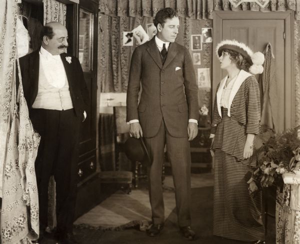 In this scene still for the 1914 silent drama "Behind the Scenes" are, from left to right, Russell Bassett playing the theatrical producer Joe Canby, James Kirkwood playing Steve Hunter, and Mary Picford playing Hunter's wife, the actress Dolly Lane. The setting is Lane's dressing room in a theater.