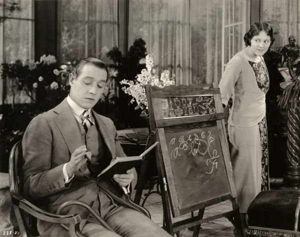 Scene still with Elliot Dexter and Mabel Julienne Scott Richard Armour, played by Elliott Dexter, sits reading a book to a child who is out of the frame as his brother's wife Lali Armour, a half-breed Indian, played by Mabel Julienne Scott, observes in a scene still for the silent drama "Behold My Wife."