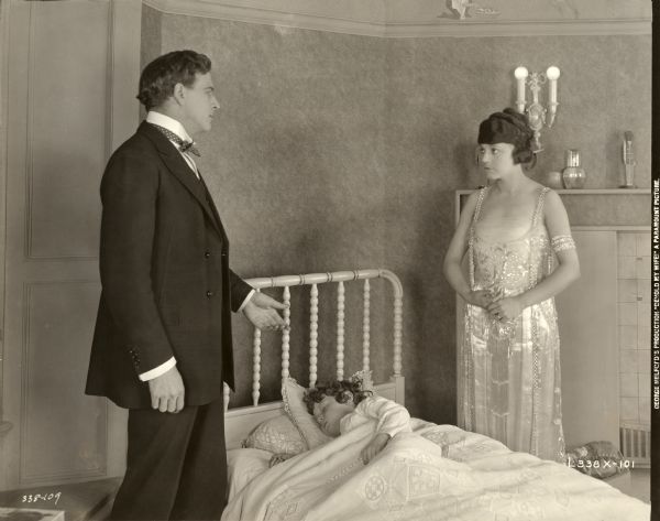 Scene still with Milton Sills and Mabel Julienne Scott in a child's bedroom Frank Armour (played by Milton Sills) and his wife Lali (Mabel Julienne Scott) stand on either side of their sleeping child's bed in a scene still for the silent drama "Behold My Wife." Scott is costumed in a beaded, white satin evening gown. The child actor is unidentified.