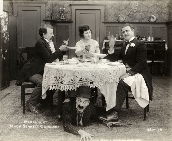 Seated around a table in a dining room, Mary Thurman offers a spoonful of peas to Ford Sterling (at right, dressed as a dandy) while Chester Conklin begs for more on the left. Hidden under the table is an unidentified actor with a long barreled revolver in this scene still for the Mack Sennett silent comedy "Beware of Boarders."