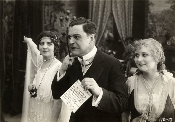 The American millionaire's daughter Julie King (played by Marguerite Snow, left) shows the way out to J. Courtleigh Brice (Harry Benham in a monocle) to the amusement of Princess Sonia (Ethyle Cooke) in a scene still from the Thanhouser silent comedy "Daughter of Kings." The note Brice holds reads, "Mr. A. Courtleigh Brice: Sir: No member of the King family would demean herself by marrying a man who is a traitor to her country. So go back to Europe and stay there. Yours with emphasis, Theo. King."